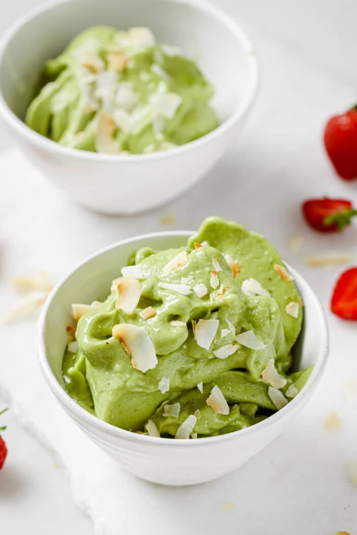 matcha nice cream in two white bowls sprinkled with coconut flakes on a white backdrop