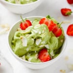matcha nice cream in two white bowls, sprinkled with coconut flakes and topped with fresh strawberries on a white backdrop