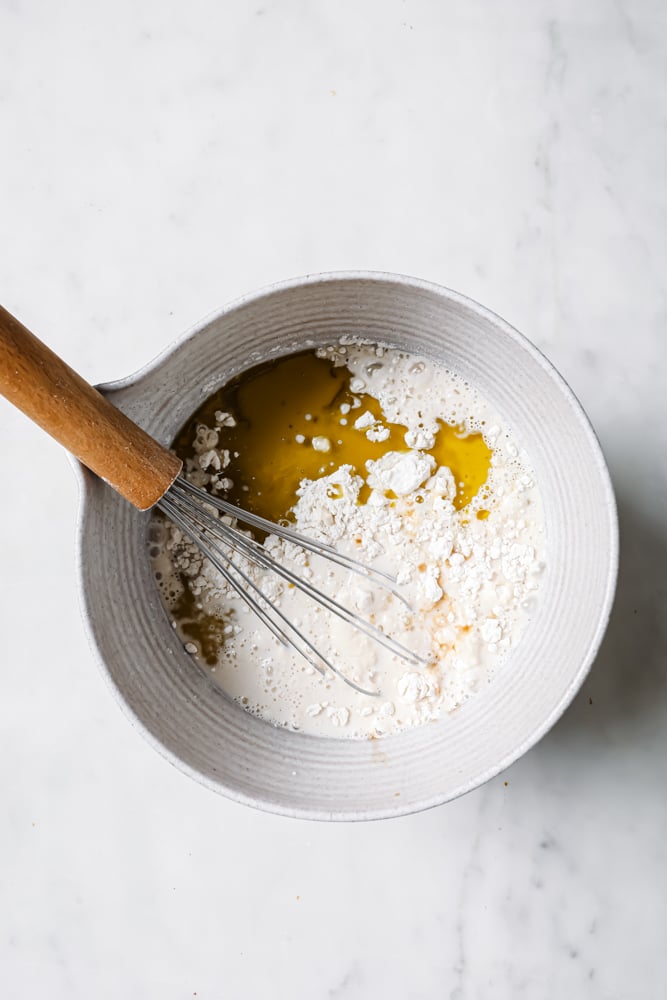 a large white bowl with crepe ingredients in the bowl that's ready to be stirring with a whisk. The white bowl is sitting on a white backdrop.