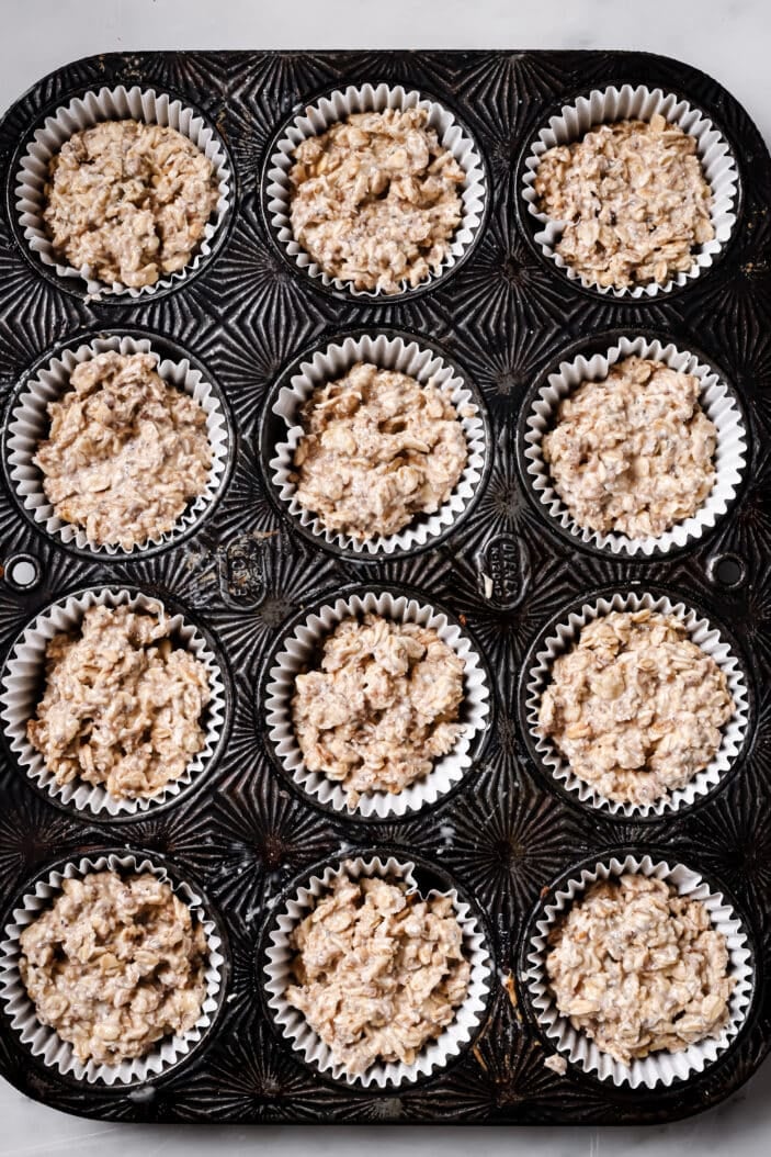 The batter to make healthy raspberry oat muffins scooped into a muffin tray. The tray is lined with white muffin liners. 