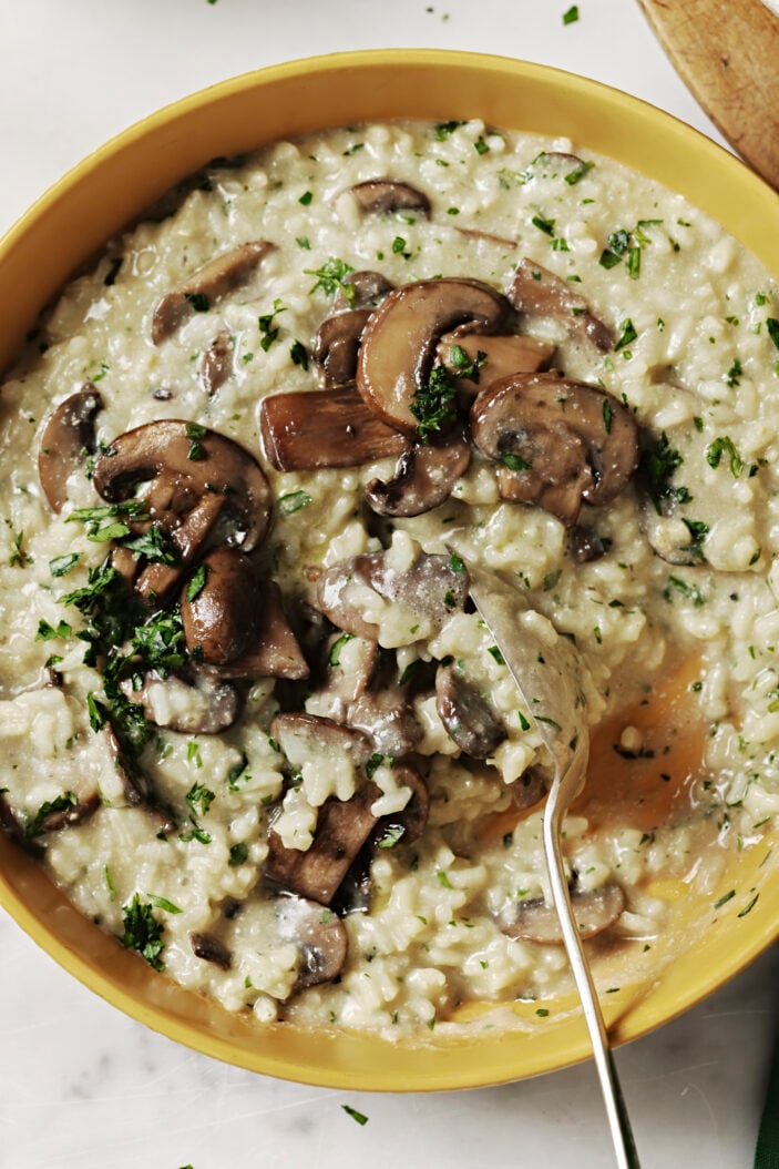 bowl of vegan mushroom risotto being scooped with a spoon showcasing the deliciously creamy and thick consistency.