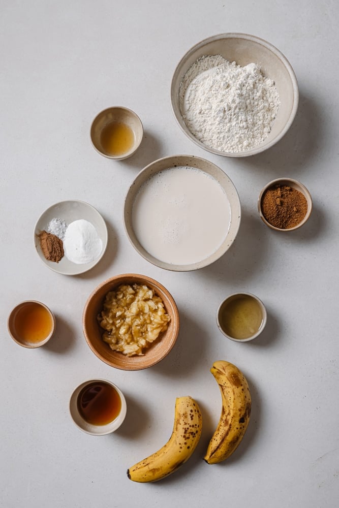 All of the ingredients to make the fluffy vegan pancakes separated into individual bowls. The bowls are sitting on a white backdrop.