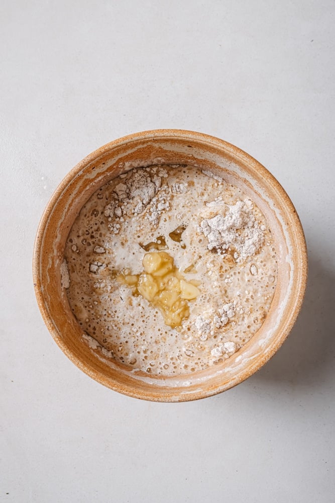 All of the wet ingredients to make the fluffy vegan pancakes poured into the flour mixture. The batter is in a brown bowl. The bowl is sitting on a white backdrop.