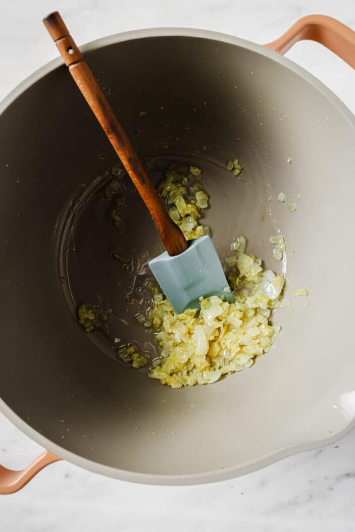 image of onion and garlic cooking in a saucepan with a spatula for stirring