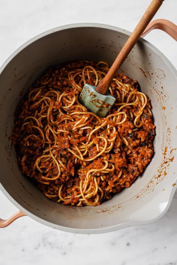 lentil bolognese stirred into spaghetti noodles in a saucepan