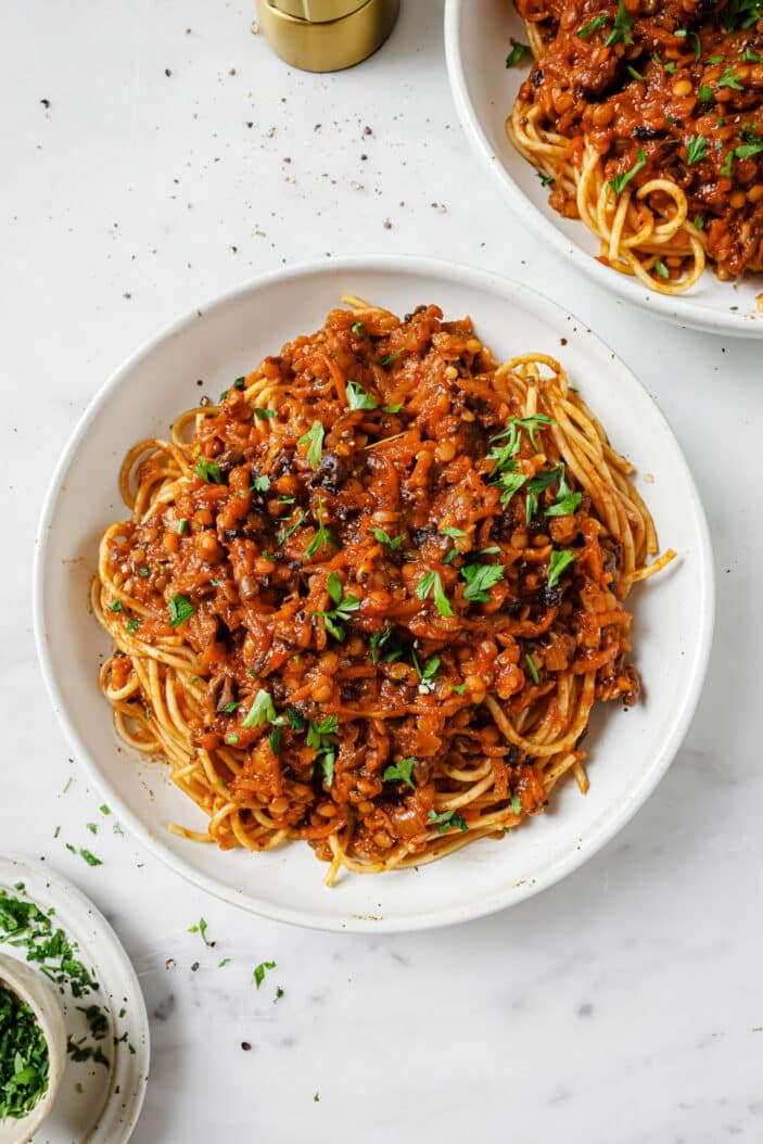 top down visual of the lentil bolognese in a white bowl with spaghetti noodles on a white backdrop