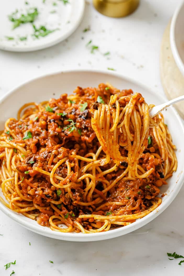 side angle of lentil bolognese with a fork that's twirled some of the spaghetti and is lifting it out of the bowl