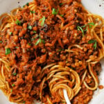lentil bolognese scooped on top of spaghetti noodles in a white bowl with a fork that's twirled spaghetti noodles around it.