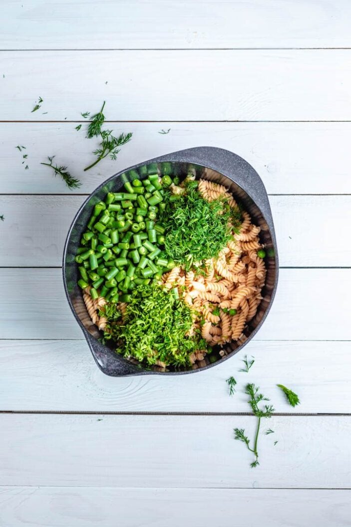 Chickpea pasta in a large mixing bowl with chopped green beans, peas and green onion