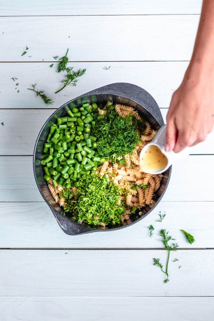 A delicious lemon vinaigrette being poured over chickpea pasta salad in a large mixing bowl