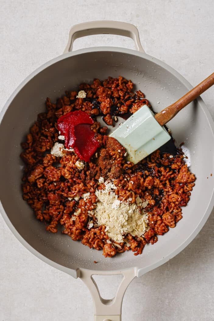 The plant-based ground with the spices and condiments added to the plant-based ground for making flavourful vegan taco meat. The mix is on a skillet with a spatula on a white backdrop.