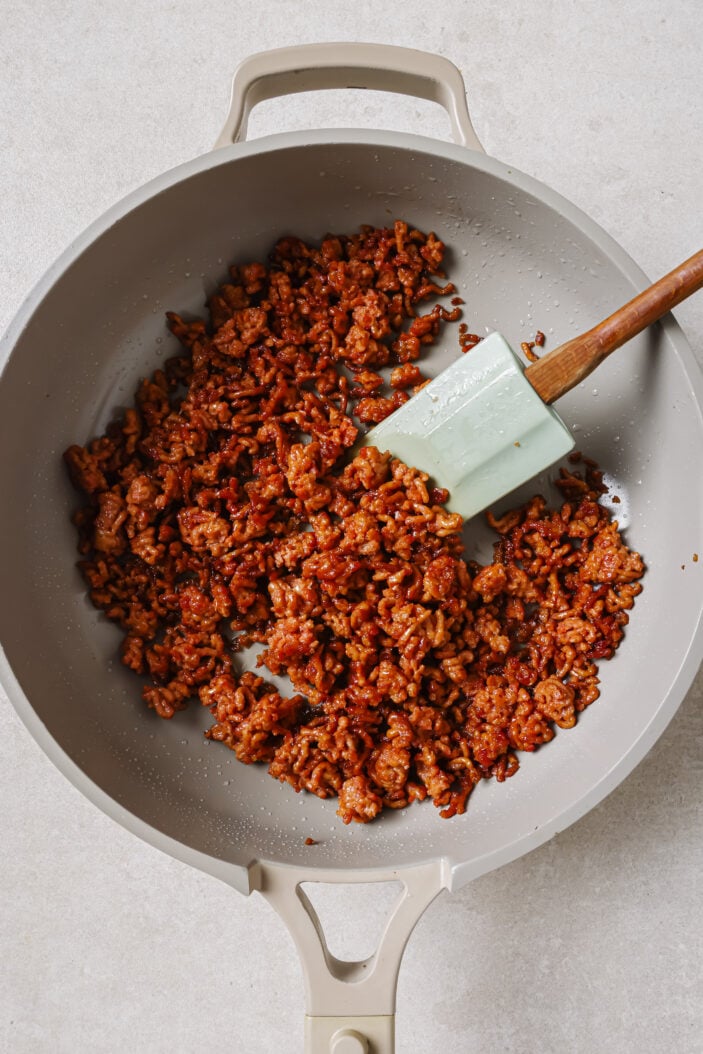 The plant-based ground to make a vegan taco. The plant-based ground is in a grey skillet with a spatula on a white backdrop.