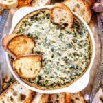 spinach and artichoke dip served in a round baking dish with toasted baguette