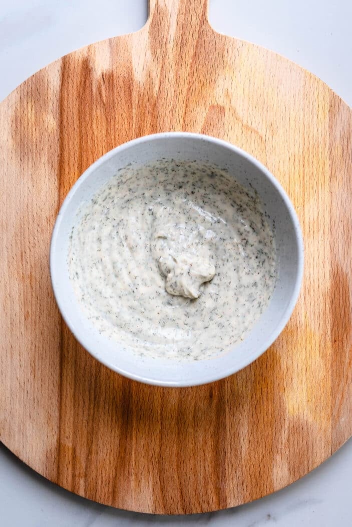 vegan ranch dip with the ingredients having been mixed together for a smooth consistency. Showcased in a white bowl with a wood cutting board