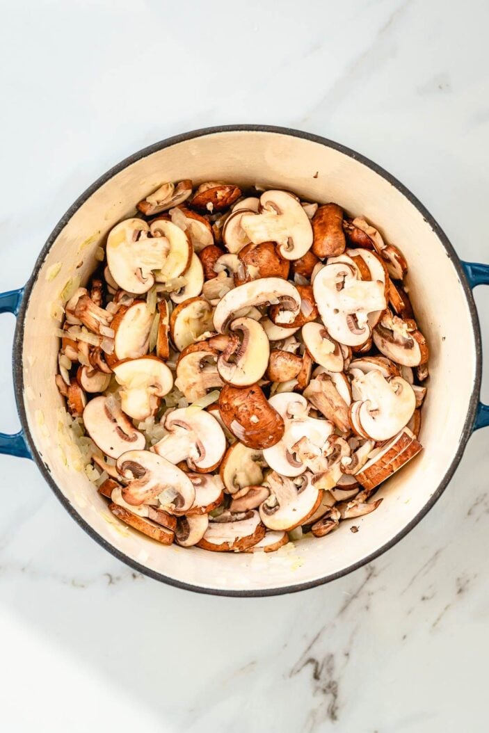 softened onions and sliced mushroom in a large pot on a marble counter top.