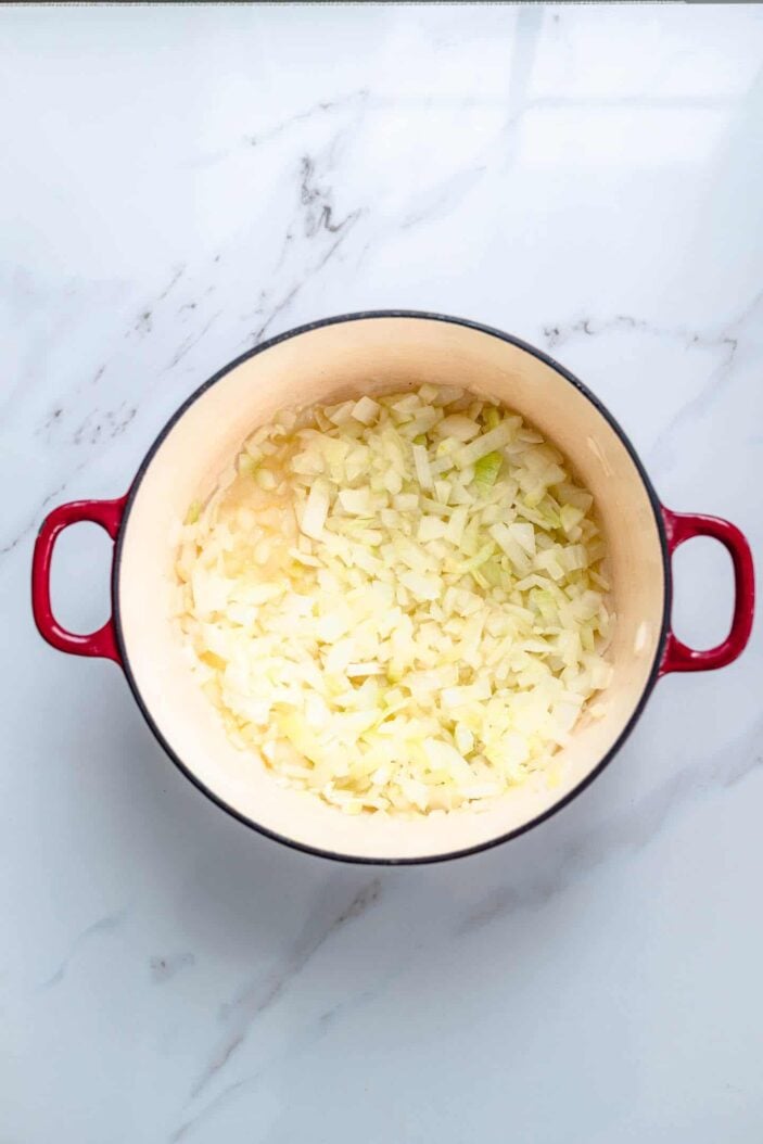 Sautéed onion and garlic in a red dutch oven. The dutch oven is sitting on a white backdrop.