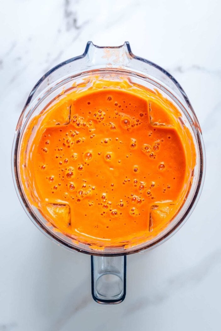 All of the ingredients to make the vegan tomato basil soup blended together. The soup is in a blender container. The container is sitting on a white backdrop.