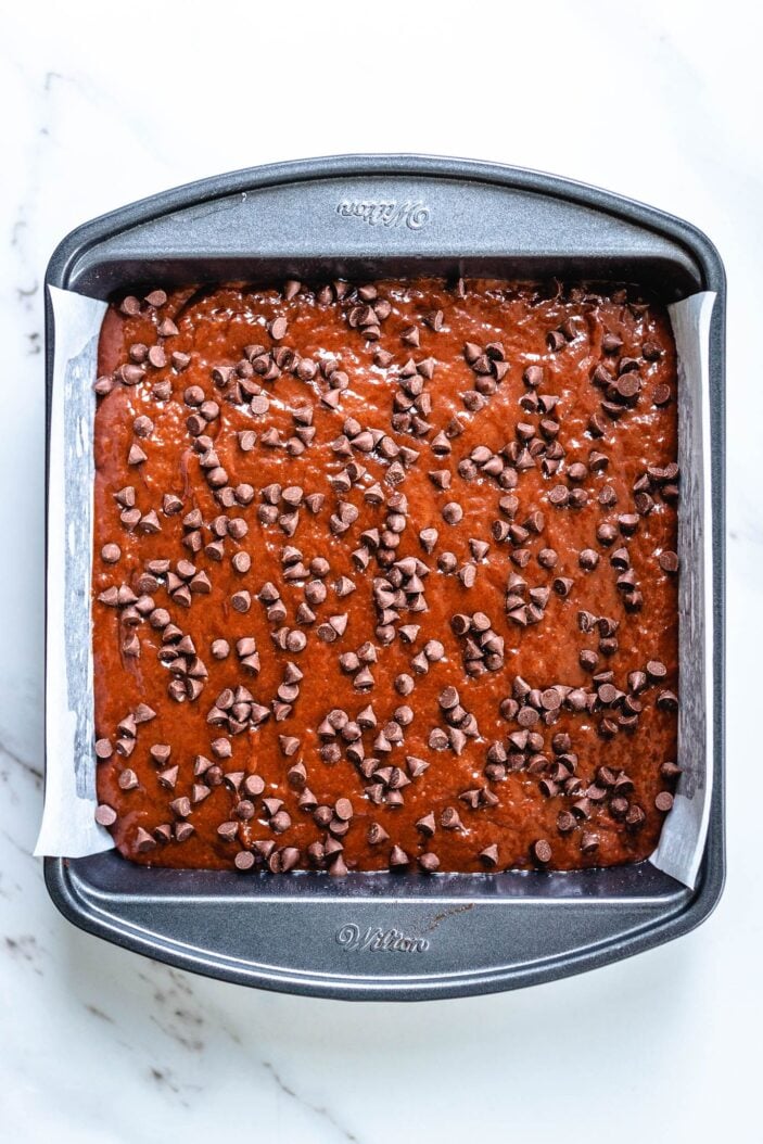Brownie batter in a square baking tin sprinkled with chocolate chips.
