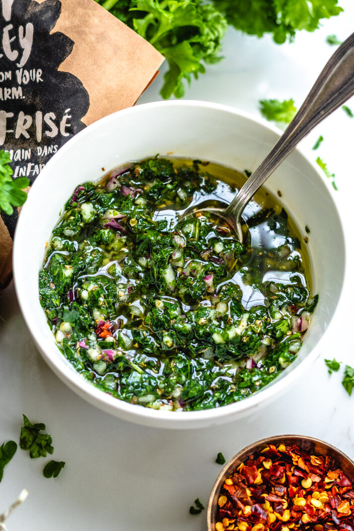 image of chimichurri in a white bowl with a spoon in the middle.