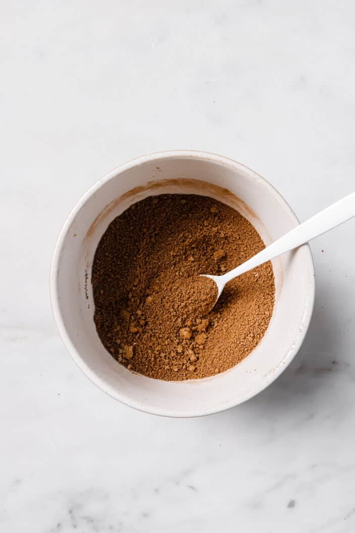 Brown sugar and cinnamon mixture in a white bowl with a white spoon in the middle.
