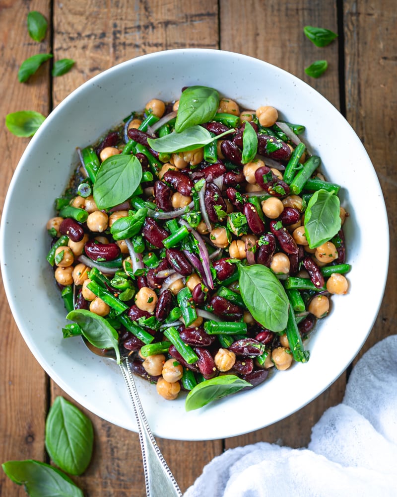 3 bean salad in a white bowl topped with fresh herbs.