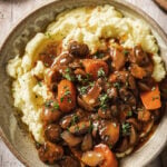 mushroom bourguignon on top of a bowl of mashed potatoes on a wood backdrop.