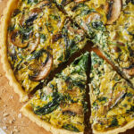 image of vegan quiche with slices cut out of it sitting on a wood cutting board