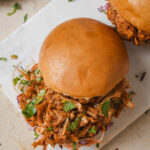 vegan jackfruit pulled pork sandwiches between two burger buns and sprinkled with cilantro