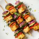 close up of 3 tofu skewers on a white plate that's been sprinkled with fresh parsley