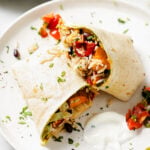 image of vegan burritos with black beans, sweet potato and rice in the filling. The burrito is cut in half to showcasing the inner filling and it's sitting on a white plate.