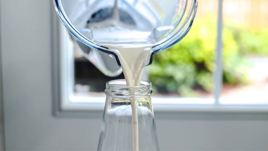 smooth and creamy almond milk being poured into a glass jar from the blender jug.