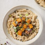 savoury steel cut oats with roasted squash on top sprinkled with microgreens. The oatmeal is in a white bowl on a white countertop.