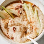amaranth porridge in a white bowl topped with sliced pears and toasted pecans. There is a spoon in the bowl ready to enjoy the porridge.