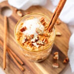 pumpkin overnight oats in a glass topped with coconut yogurt and chopped pecans with a cinnamon stick tucked in to the side of the glass.