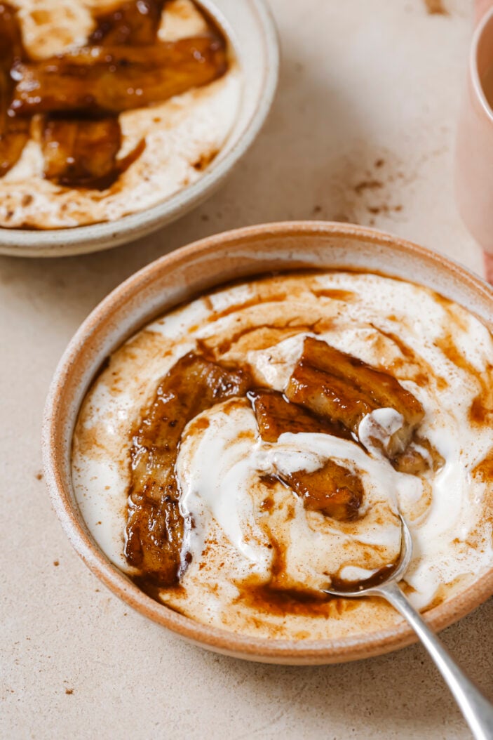 Image of caramelized bananas and coconut yogurt in a brown bowl on a light brown backdrop. There is an image of the caramelized bananas and coconut yogurt in the top left hand corner.