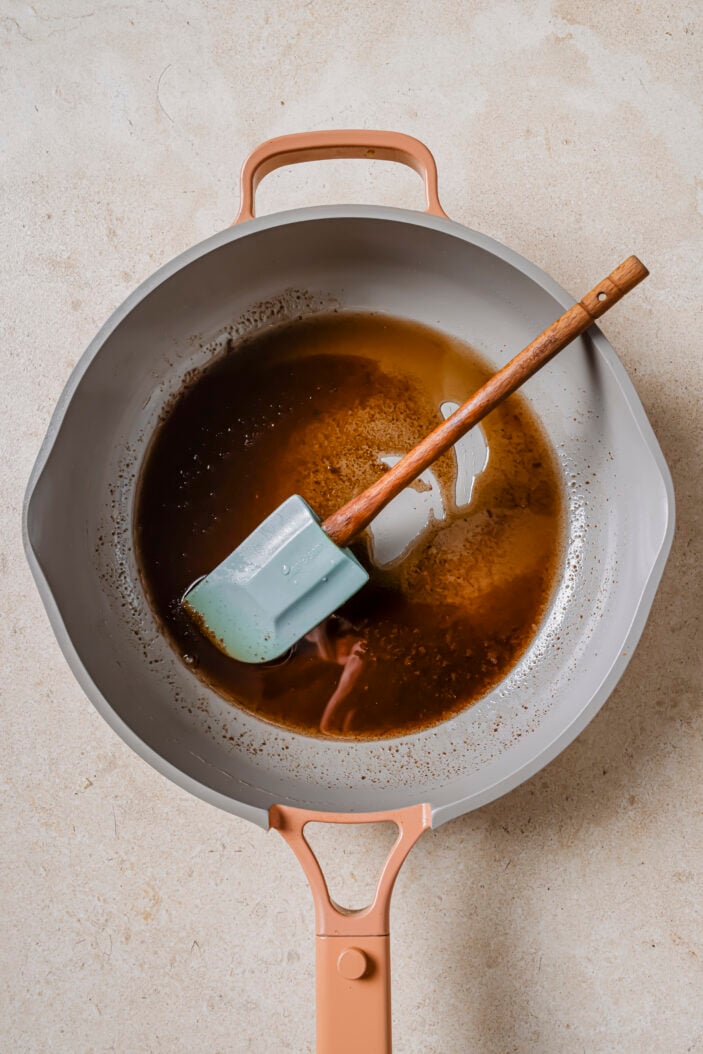 image of melted coconut oil and coconut sugar in a skillet. There is a spatula in the skillet. The skillet is sitting on a grey backdrop. 