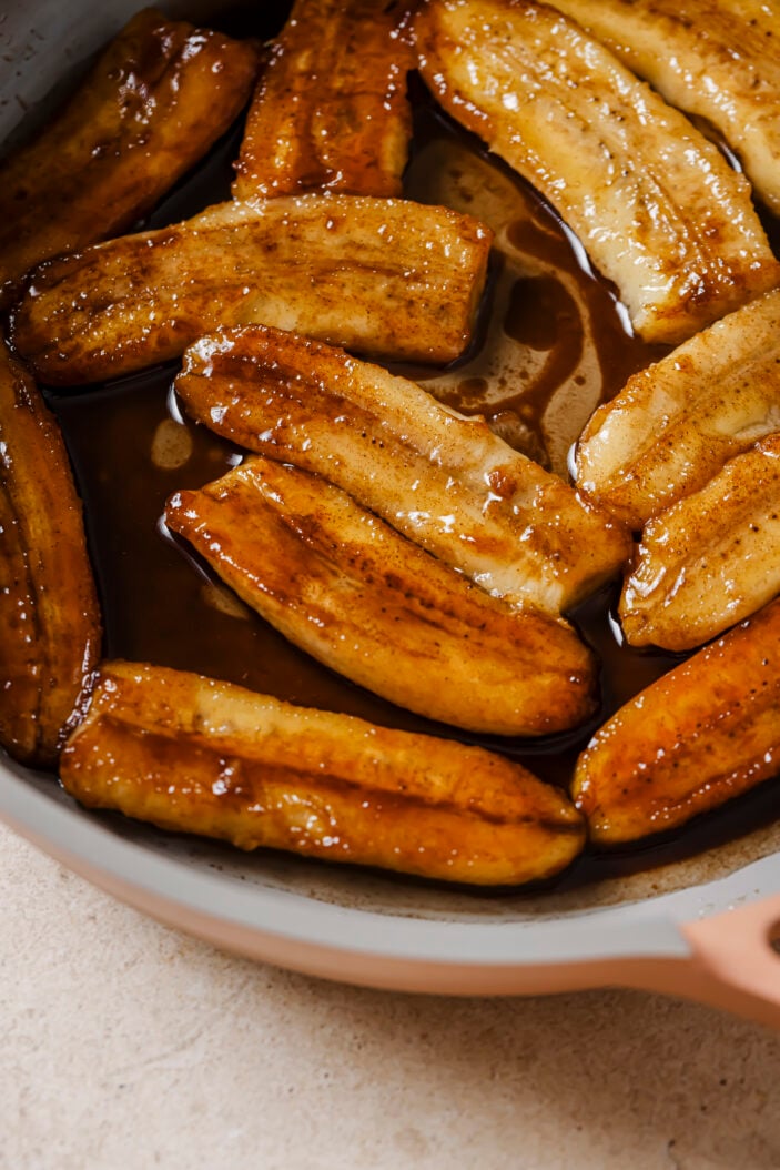 Close up of the caramelized bananas in a skillet. The skillet is on a grey backdrop. 
