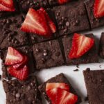 coconut flour brownies cut into squares on a white surface. Topped with fresh cut strawberries.