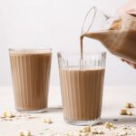 chocolate oat milk poured into two glasses on a cream backdrop