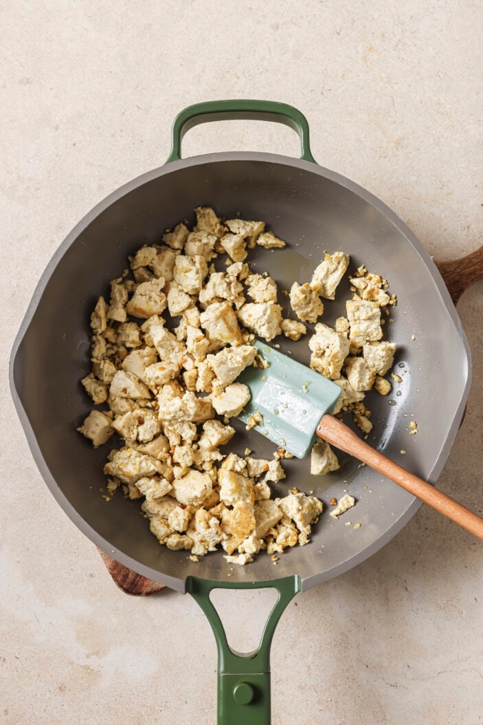 tofu crumbled into a skillet with a wooden spatula in the middle