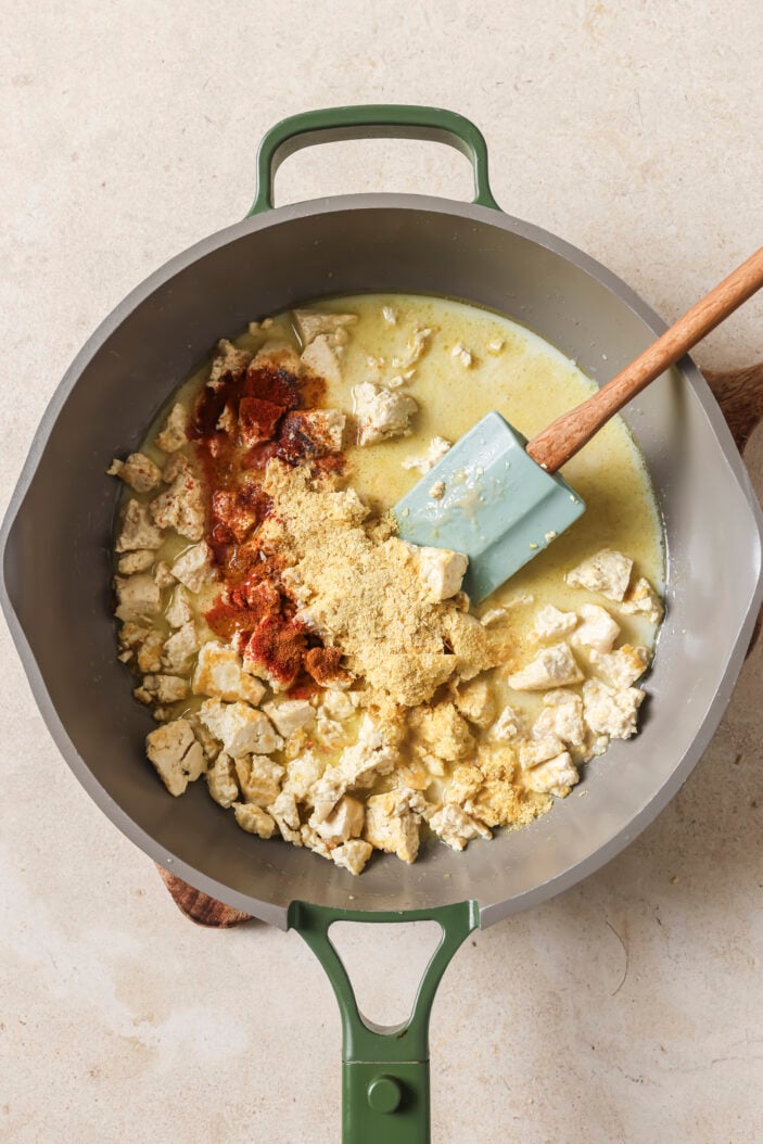 tofu crumbled into a skillet with oat milk and spices, and with a wooden spatula in the middle