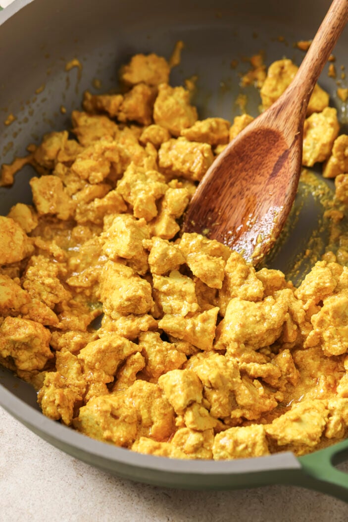 tofu scramble in a skillet with a wooden spoon in the middle.