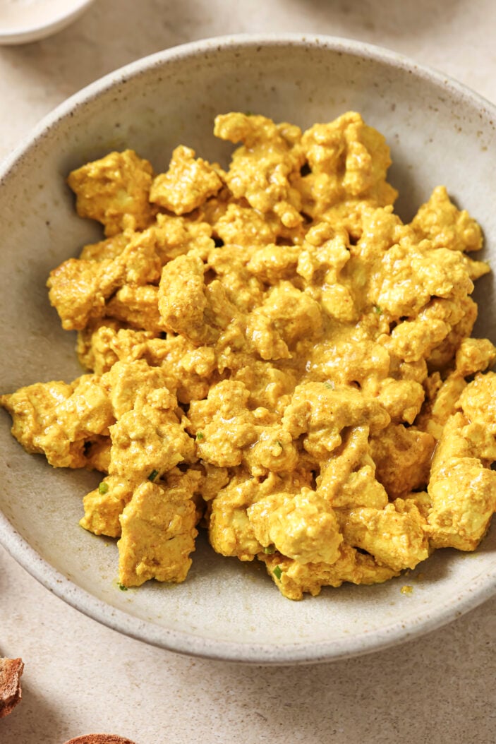 image of vegan tofu scramble in a white bowl showcasing eggy and creamy consistency.