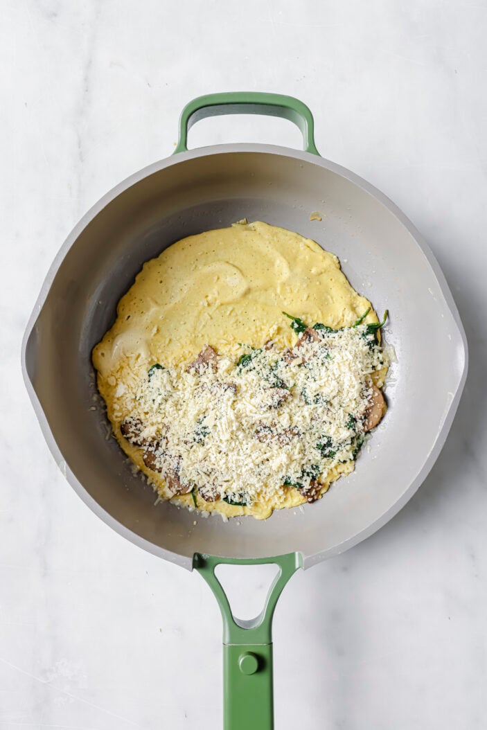 tofu omelette in a skillet with half of it spread with mushroom spinach and vegan cheese.