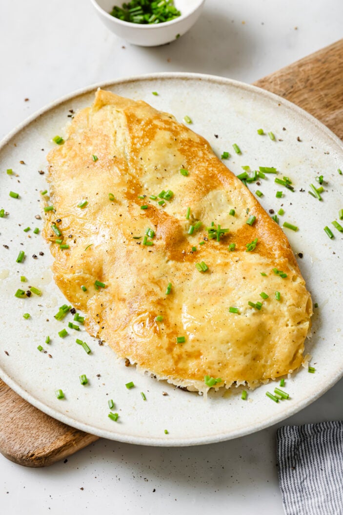 Stuffed tofu omelette served on a white plate on top of a wood cutting board. Sprinkled with fresh chopped chives.