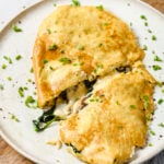 tofu omelette on a white plate stuffed with vegan cheese, spinach and mushroom. The omelette is sliced in half and sprinkled with fresh chopped chives.