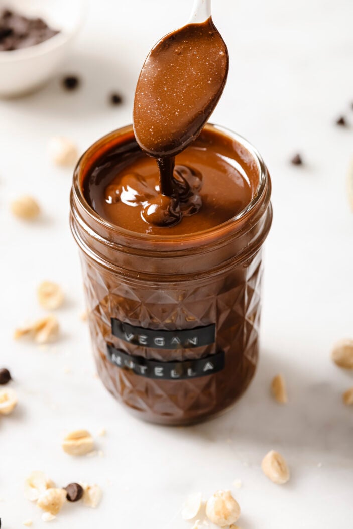 vegan nutella in a jar with a spoon scooping out the drizzly nutella