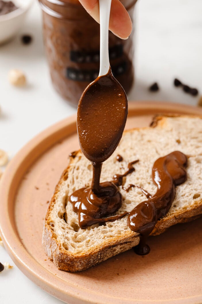 vegan nutella being drizzled onto toast sitting on a pink plate.