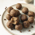 image of energy balls stacks onto a plate. One of the energy balls has a bite out of it to show the soft and chewy interior.