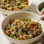 Two white bowls with crispy rice salad with roasted squash and kale. The bowl in front has a fork being scooped into it.